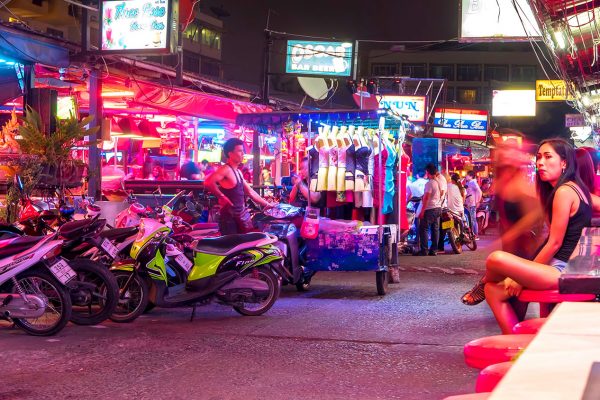 Passanti davanti alle insegne luminose dei bar di Pattaya, di notte