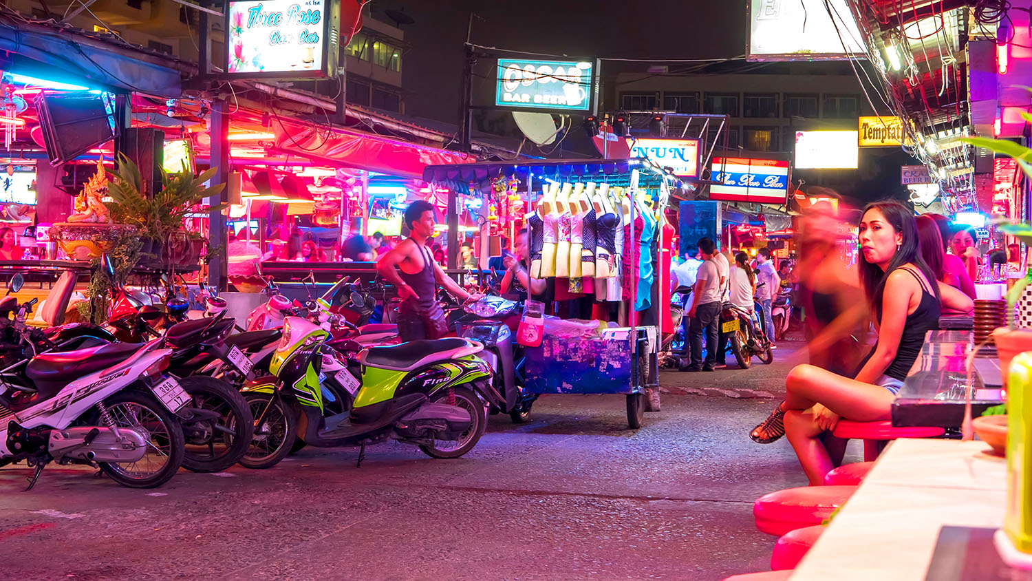 Passanti davanti alle insegne luminose dei bar di Pattaya, di notte