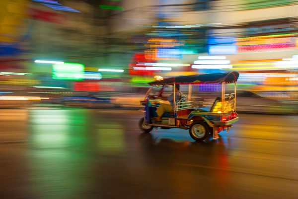 Un tuk-tuk in corsa fra le luci al neon di una strada di Bangkok di notte