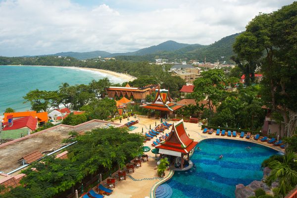 Una baia di Phuket vista dall'alto, con la piscina e i tetti thai di un resort in primo piano e la spiaggia sullo sfondo